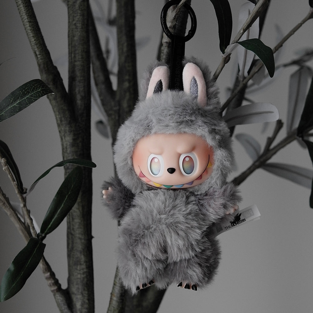 Plush toy character hanging from branches with a neutral background