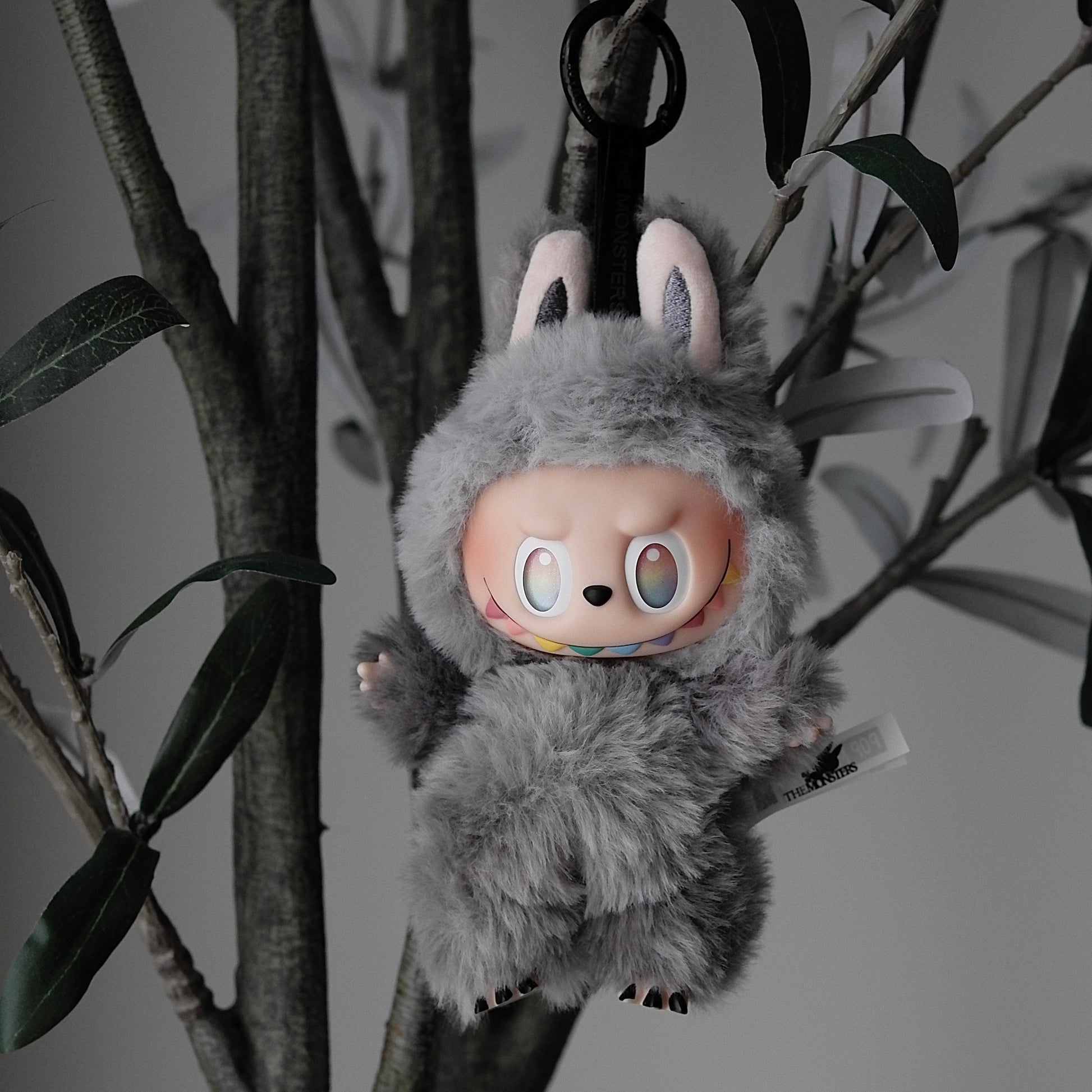 Plush toy character hanging from branches with a neutral background
